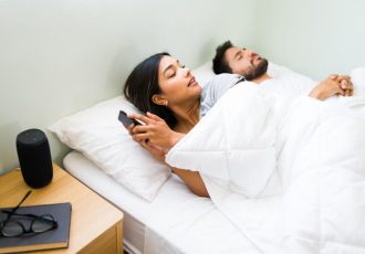 Frau benutzt Smartphone neben schlafendem Mann im Bett.
